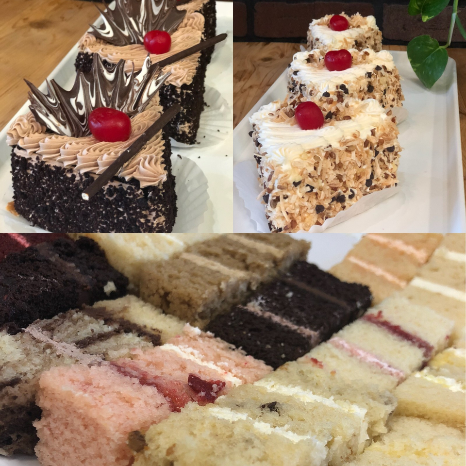 Assorted decorated cakes and colorful dessert squares displayed on white plates, including chocolate cakes topped with cherries.