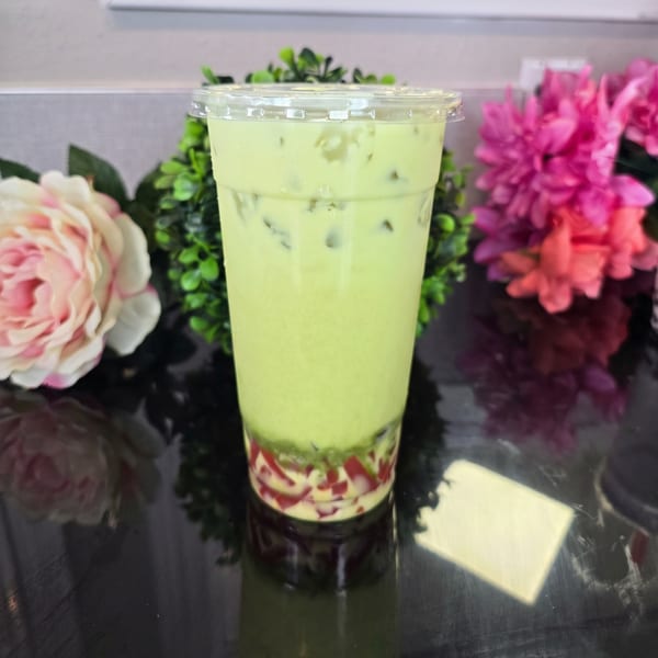 Green iced drink with red and white jelly at the bottom, surrounded by flowers.