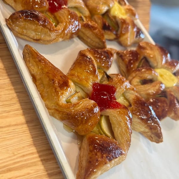 Golden-brown pastries with fruit fillings, some with red jelly and others with yellow cream, on a white tray.