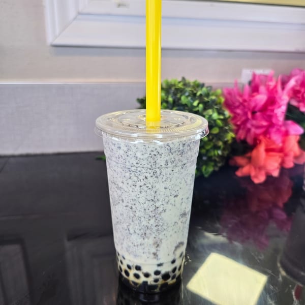 Oreo boba tea with a yellow straw, black tapioca pearls, and pink flowers in the background.